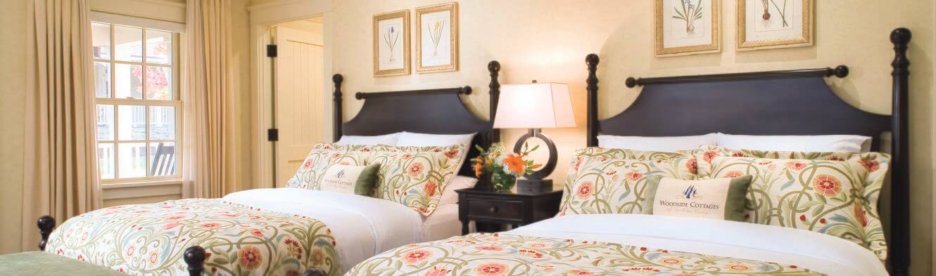 Two neatly made queen size beds lined up next to one another inside of the Woodside Cottages