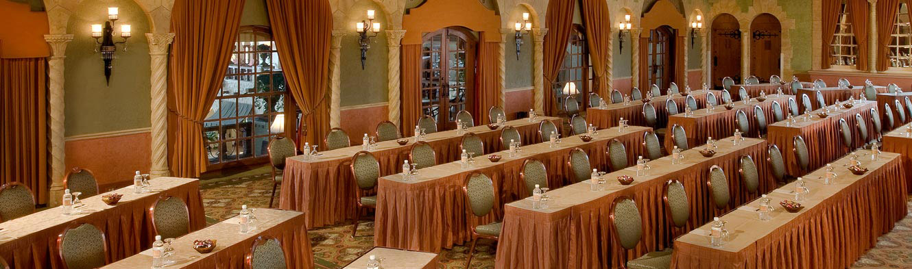 Room with large open windows and rows of long tables lined up with chairs, facing the front of the room.