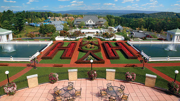 Drone shot of the formal gardens where giant two H's are formed with shrubery, also overlooking two large fountains, a balcony with outdoor seating, and fresh flowers planted around the property.