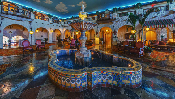 Nightime shot of Fountain Lobby in the middle of the hotel, with fountain in the middle of the room, outdoor seating, and open arcs lined on the outside of the building.