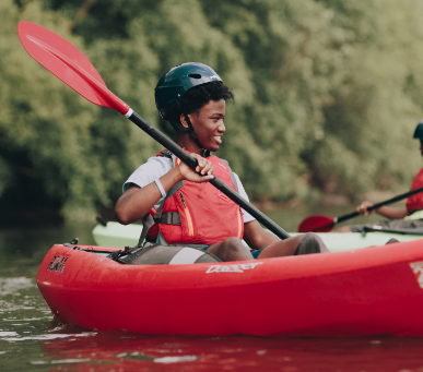 Young boy steering red kayak on water with friends
