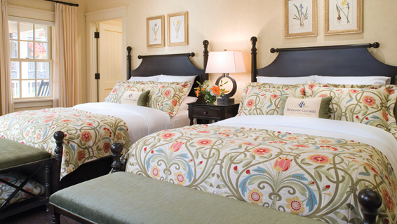 Two neatly made queen size beds lined up next to one another inside of the Woodside Cottages