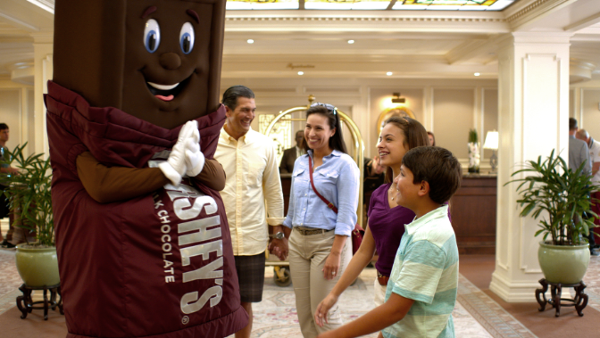 Family of four engaging in joyful conversation with Hersheypark character, Hershey's, inside of the hotel main lobby.