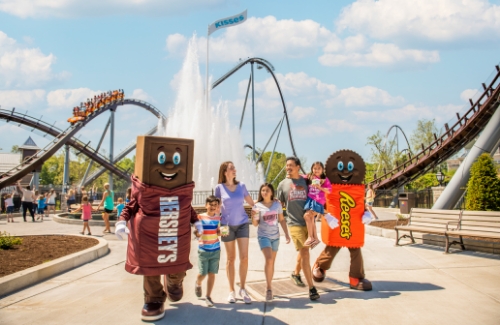 Family walking in amusement park in front of Candymonium roller coaster with Hershey's characters