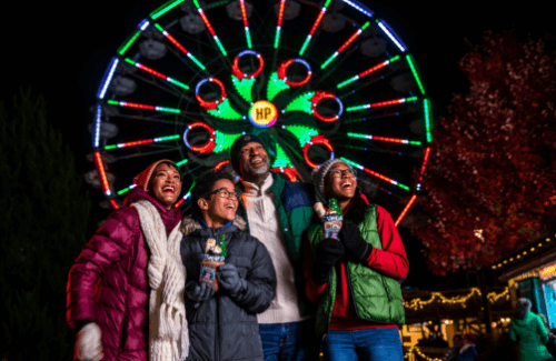 Family enjoying Hersheypark Christmas Candylane in front of ferris wheel lights