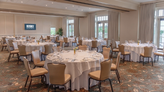 Large meeting room room with nine tables neatly decorated with white tableclothes and topped with waters, fresh fruit, and Hershey bars on the tables.