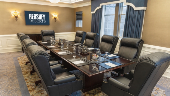 Dimmed meeting room with one large round table with comfortable office chairs lined, the table topped with waters, candies, and notepads at each seat.