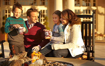 Family sitting around a fire outside The Hotel Hershey making s'mores